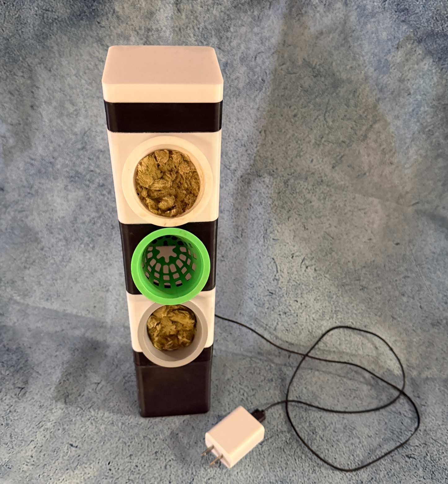 Compact countertop hydroponics unit with recirculating water system and three plant pods in black and white with green insert and USB pump.