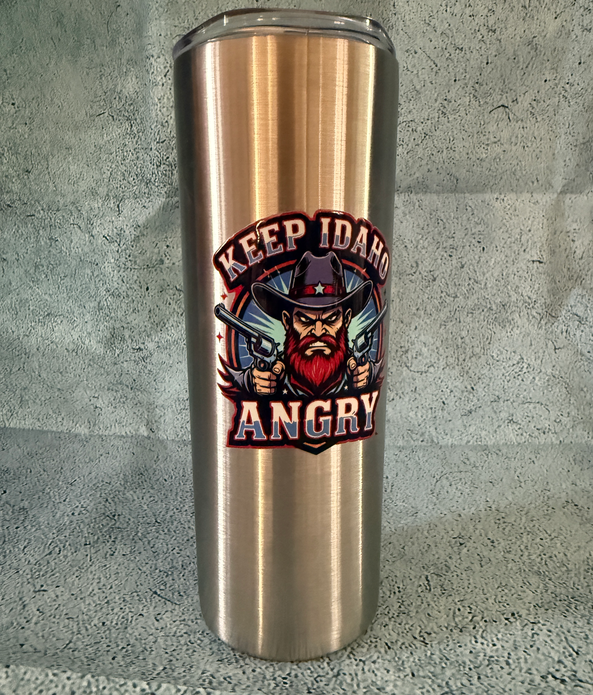 Stainless steel tumbler with 'Keep Idaho Angry' design on a gray background