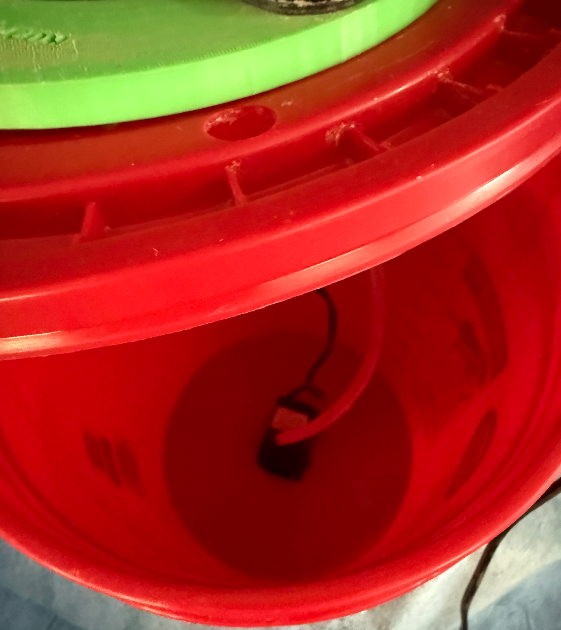 Close-up of a red plastic container with a water pump and a green lid on a gray surface.