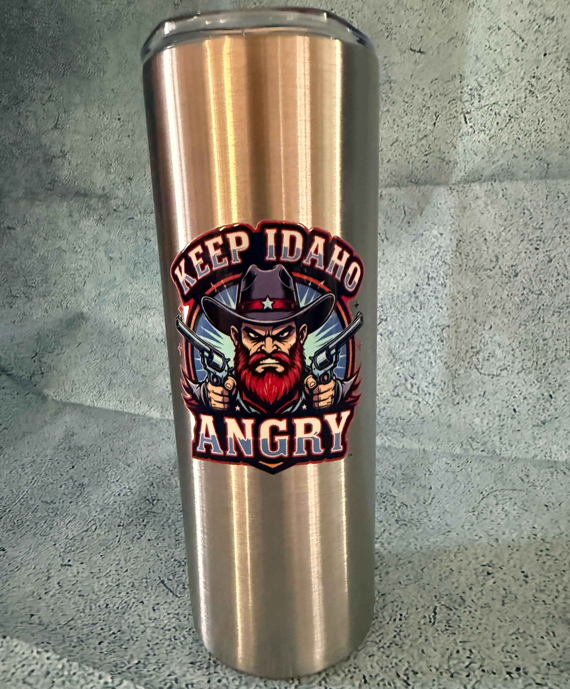 Stainless steel tumbler with 'Keep Idaho Angry' design on a concrete surface